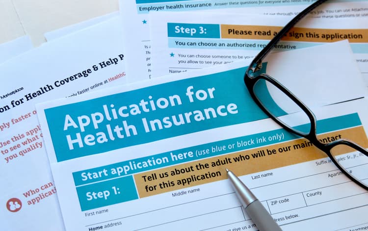 Close-up of health insurance application forms with a pen and eyeglasses placed on top, highlighting the section titled “Application for Health Insurance.”